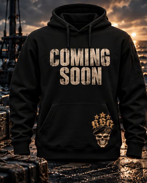 Black hoodie with Coming Soon across the chest and the RBG skull-in-beret on the hem, on a boat deck at dusk
